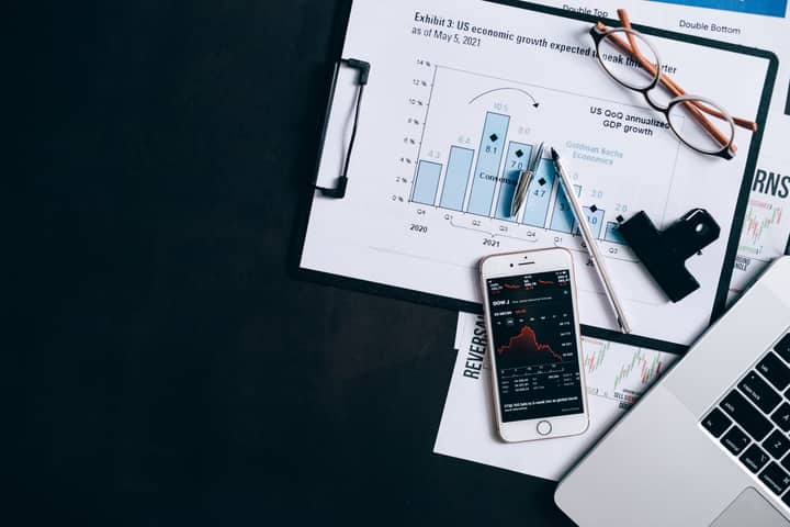 Top view of financial reports, smartphone showing stock market data, and a laptop on desk.