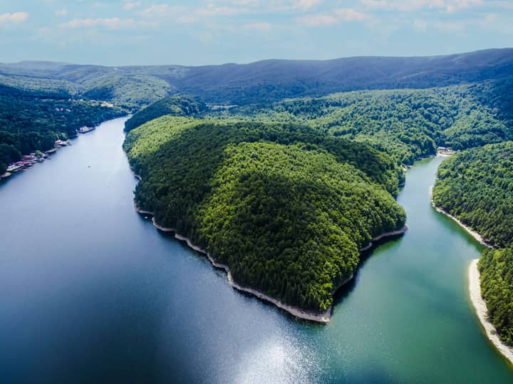 Stunning aerial view of Văliug Lake in Romania, showcasing lush greenery and serene waters.