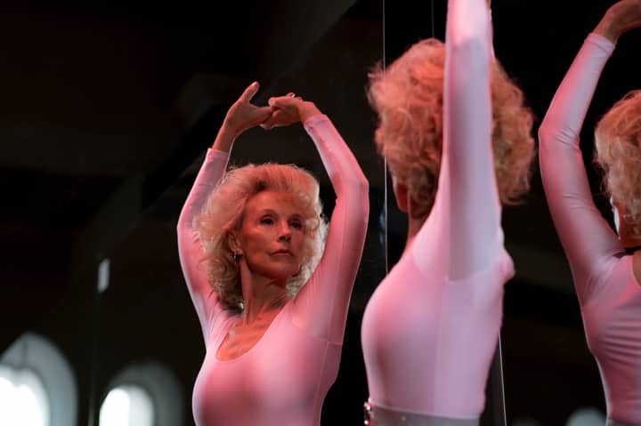 A graceful senior woman in a leotard dancing ballet indoors, showcasing elegance.