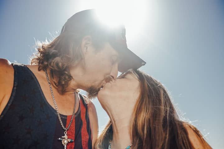 A loving couple sharing a kiss outdoors under the bright sunlight, showcasing affection and happiness.
