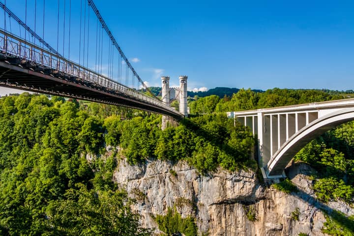 Aerial view of dual bridges spanning a lush green canyon, showcasing architectural contrast.