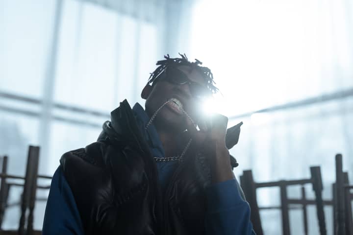 Stylish urban man in sunglasses and streetwear holding a chain indoors with bright backlight.