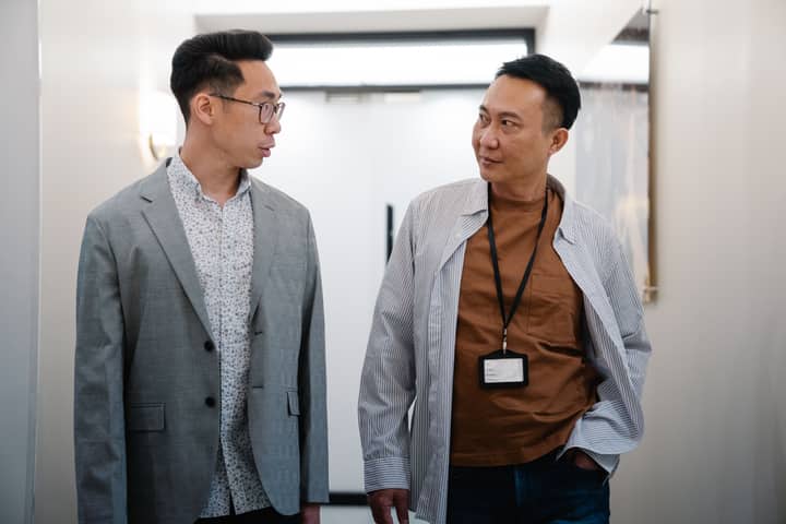 Two professional men conversing in a well-lit corridor, showcasing teamwork and cooperation.