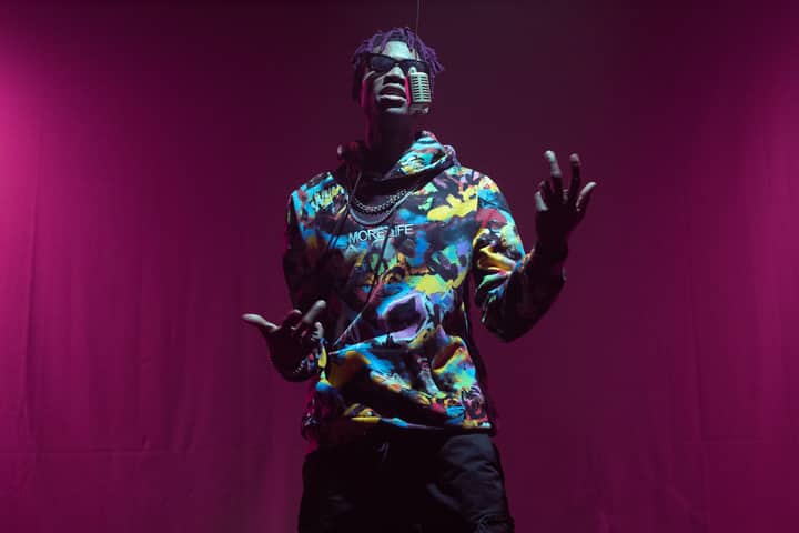 Rapper in colorful hoodie performing with mic on red stage. Captivating music and style.