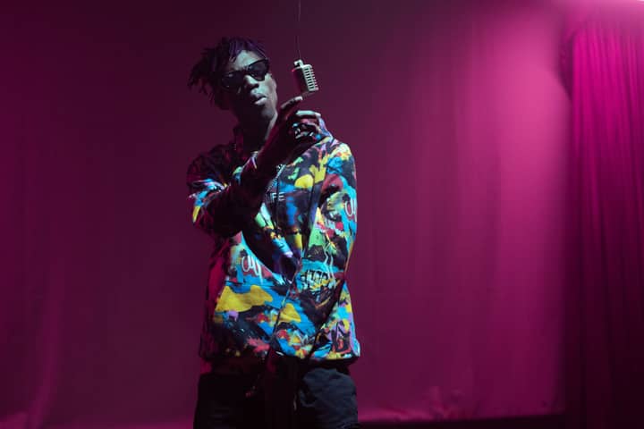 A vibrant rapper energetically performing on an indoor stage under bright lights.