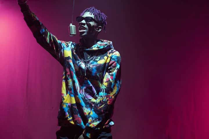 Colorful performer with vibrant hoodie singing into retro microphone on stage.