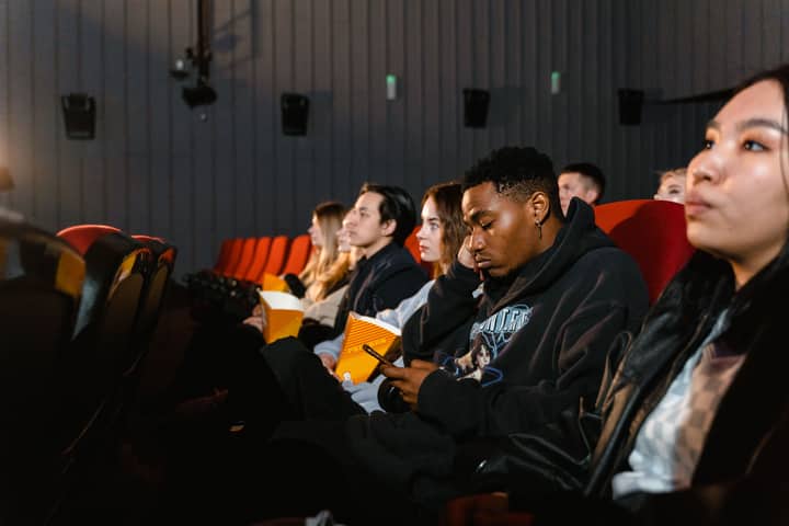A diverse group of people enjoying a movie in a theater, some focused on phones.
