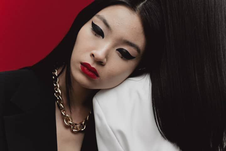 Stylish portrait of a woman with bold makeup and statement jewelry against a red backdrop.