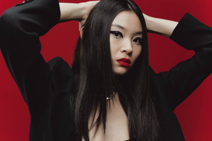 Chic portrait of a stylish young woman in a black jacket against a bold red background.