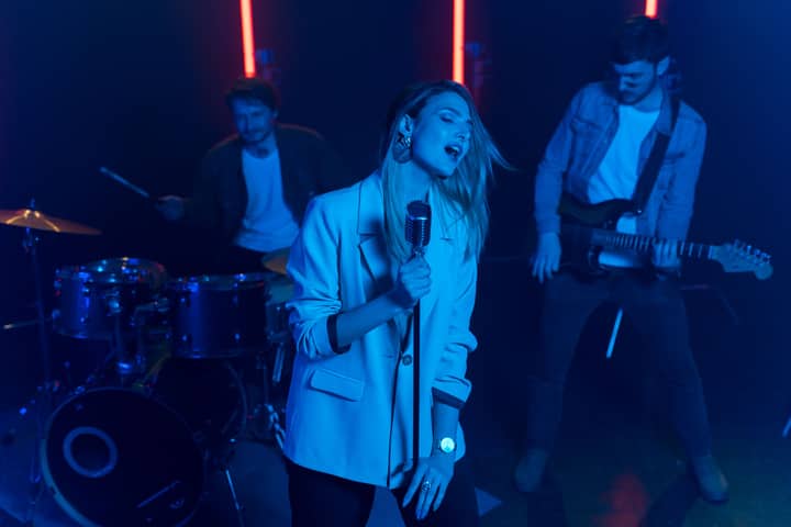 A dynamic live band performance with a female vocalist and musicians playing instruments in vibrant lighting.