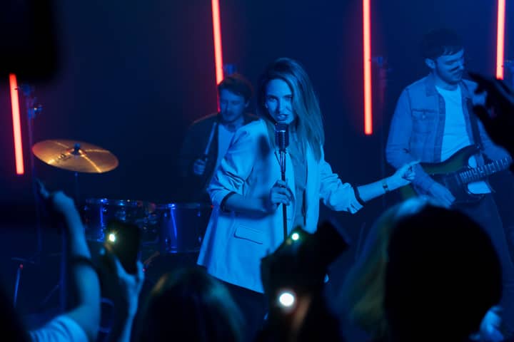 Woman singer performing with band on stage, vibrant lights, crowd enjoying the music.