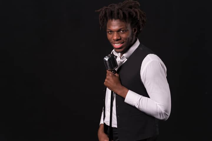 Smiling singer holding a vintage microphone against a black background.