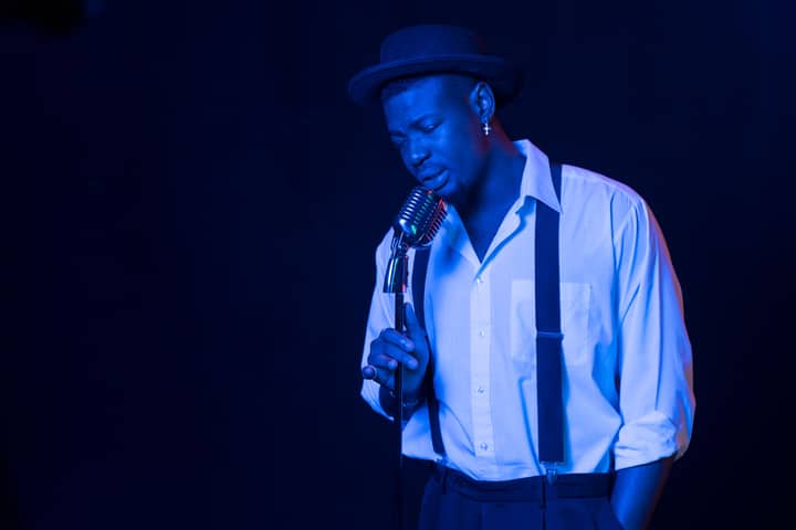 A male vocalist passionately sings under blue stage lighting, exuding emotion and style.