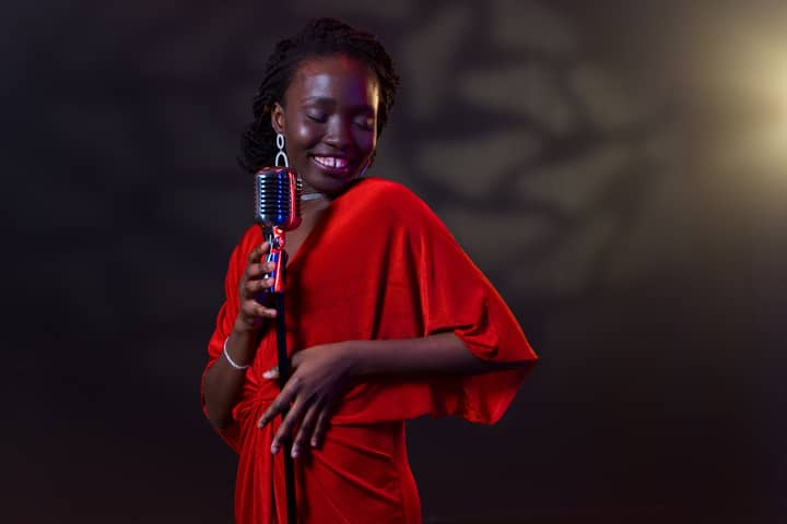 A talented black female artist singing joyfully into a vintage microphone in an elegant red dress.