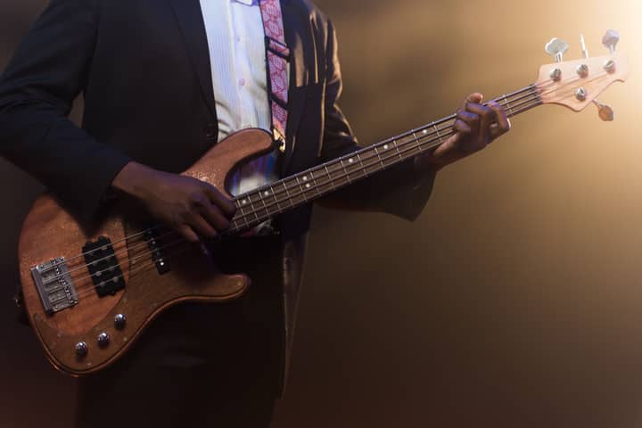 A musician in a suit playing a bass guitar on stage under warm lighting.