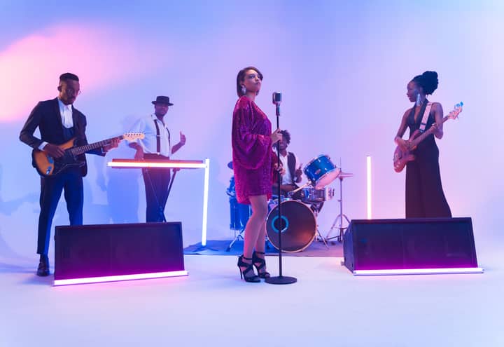 A multi-ethnic band performing live with vibrant lighting and diverse instruments.