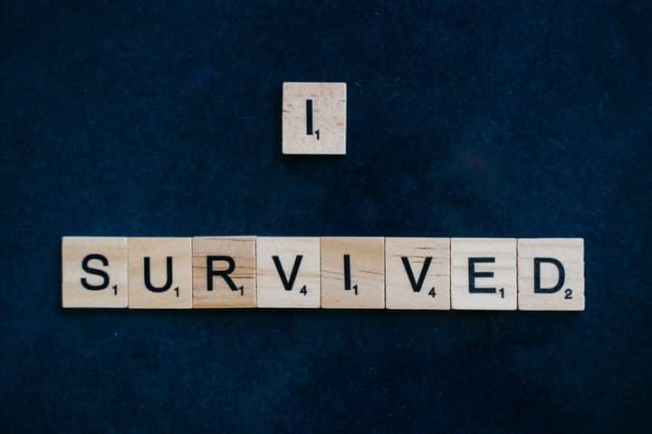 Wooden Scrabble tiles spelling 'I Survived' on a dark surface conveying strength and resilience.