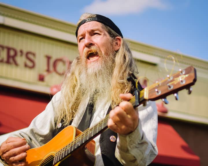 Senior man with gray hair passionately playing guitar outside a building.