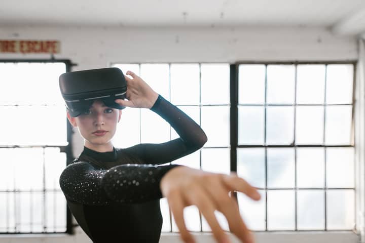 Elegant woman engaged in a virtual reality dance, wearing VR headset and black outfit.