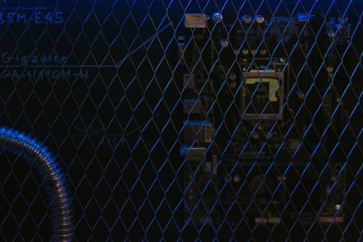 Artistic view of a circuit board through metal mesh with blue lighting.