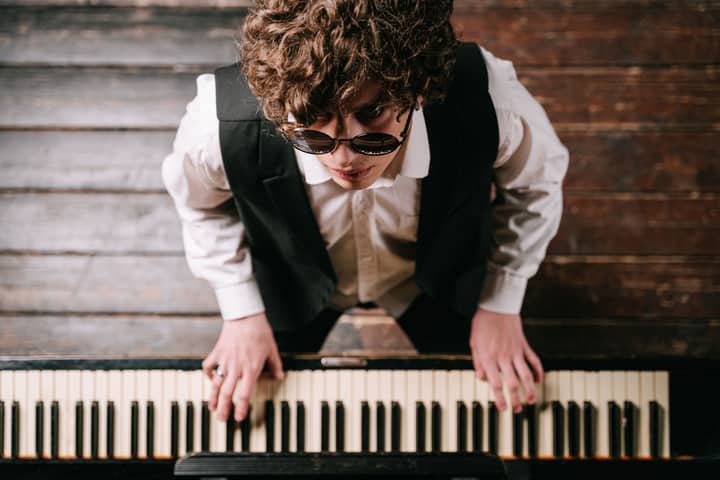 A view from above of a pianist wearing sunglasses playing the piano on a wooden floor.