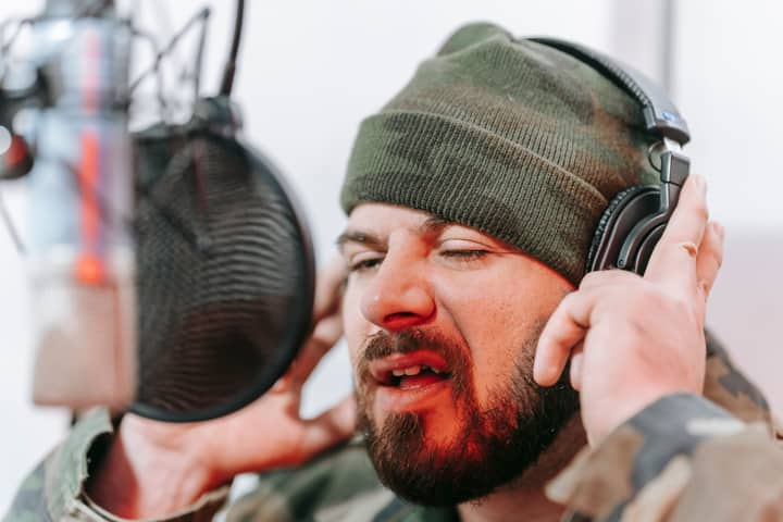 Close-up of a musician recording vocals in a studio, wearing headphones and camouflage.