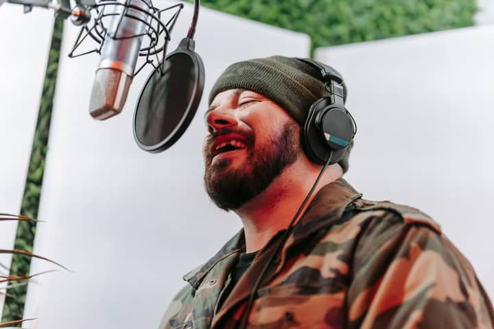 Bearded man singing passionately in a music studio with headphones and a microphone.