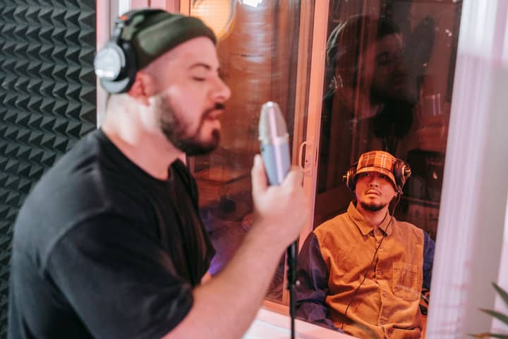 Singer recording a track in a studio with producer observing through glass. Captured in a creative music environment.