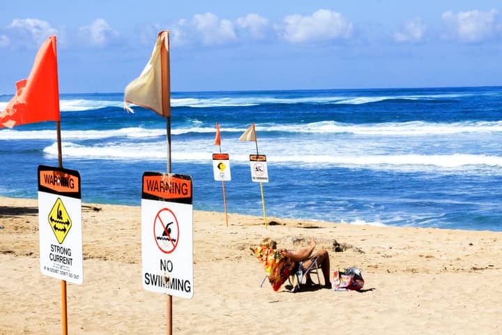 Sunny beach scene with no swimming warning signs, ocean waves, and a person relaxing.