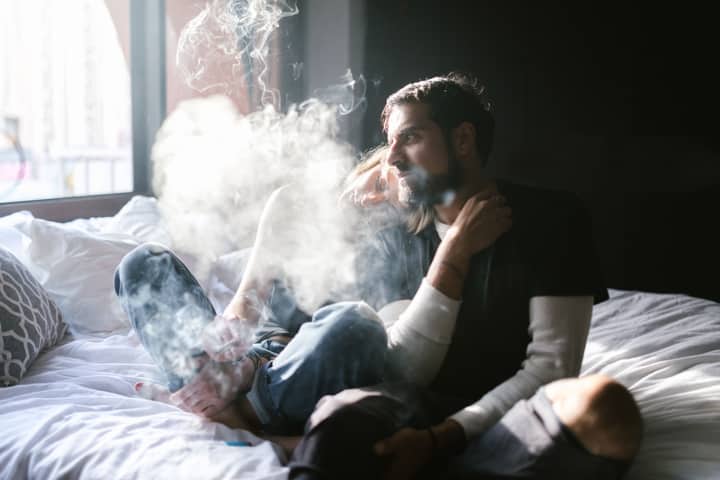 A young couple relaxing on a bed indoors, surrounded by a haze of smoke.