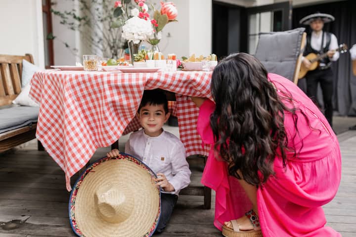 Mother and child at festive outdoor Cinco de Mayo party with traditional decor and music.