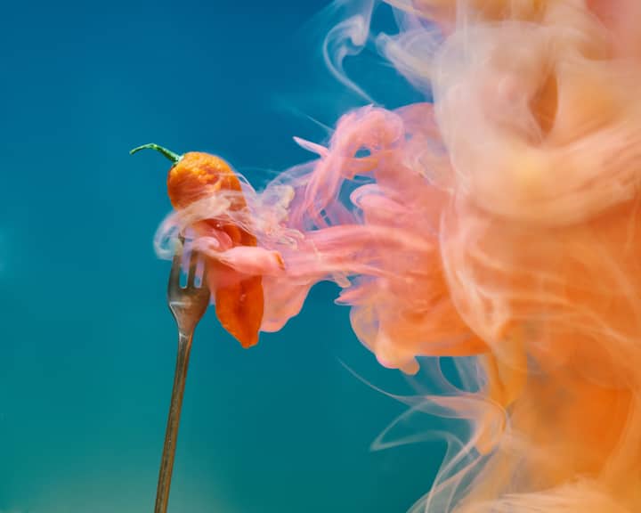 A vibrant image of a fiery pepper on a fork with dramatic swirling smoke against a gradient background.