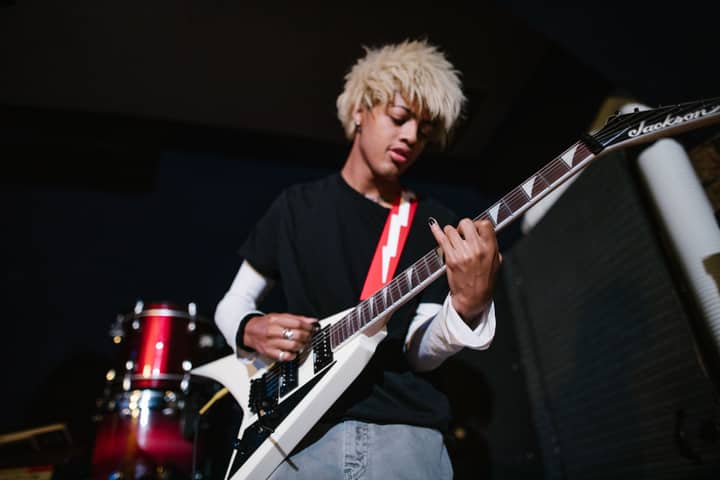 Energetic young guitarist playing a white electric guitar in a dimly lit room.