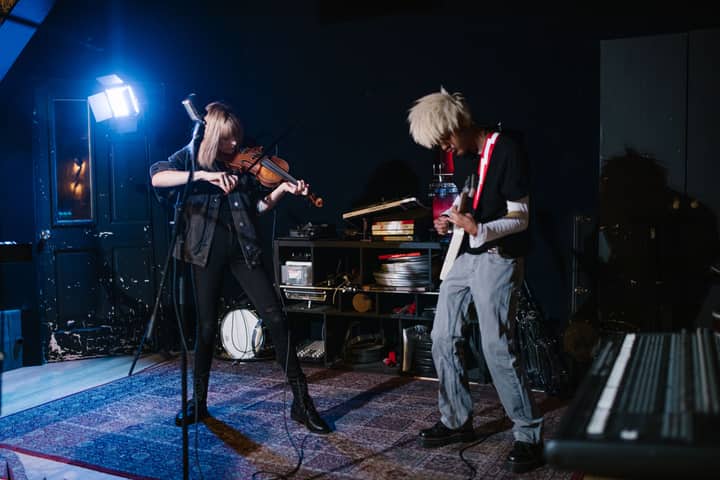 Energetic musical duo playing violin and electric guitar in a studio setting.