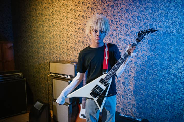 Stylish guitarist with blond hair holding an electric guitar in a recording studio.