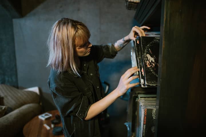 A woman in a black shirt explores a collection of vintage vinyl records on a wooden shelf indoors.