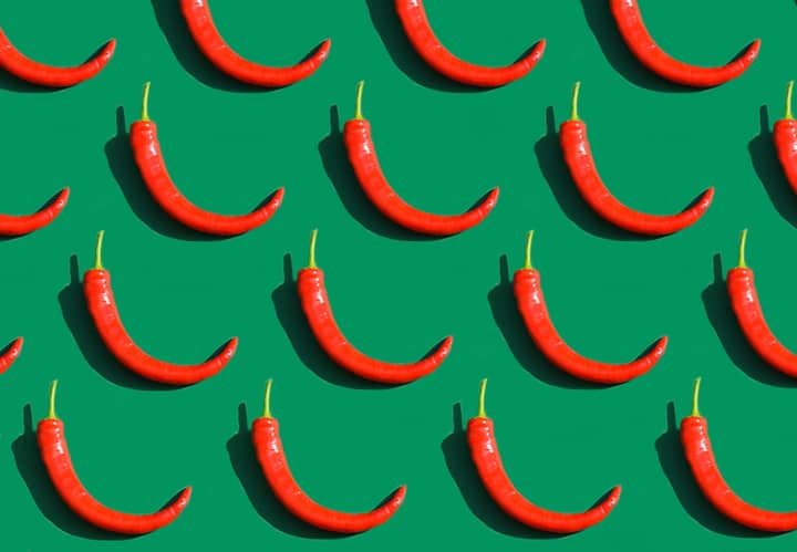 Pattern of red chili peppers on a vivid green background, emphasizing spicy and hot themes.