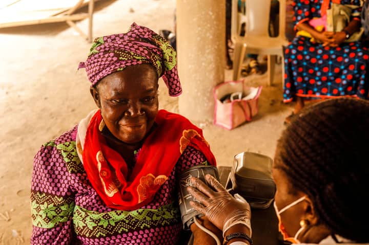 A smiling woman in traditional clothing having her blood pressure measured by a healthcare worker.