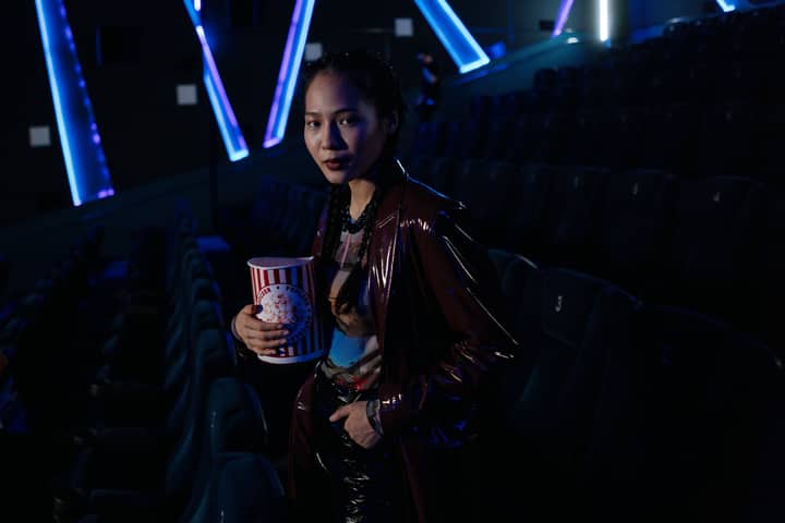 A stylish young woman holding popcorn in a dimly lit cinema, ready for a movie night experience.