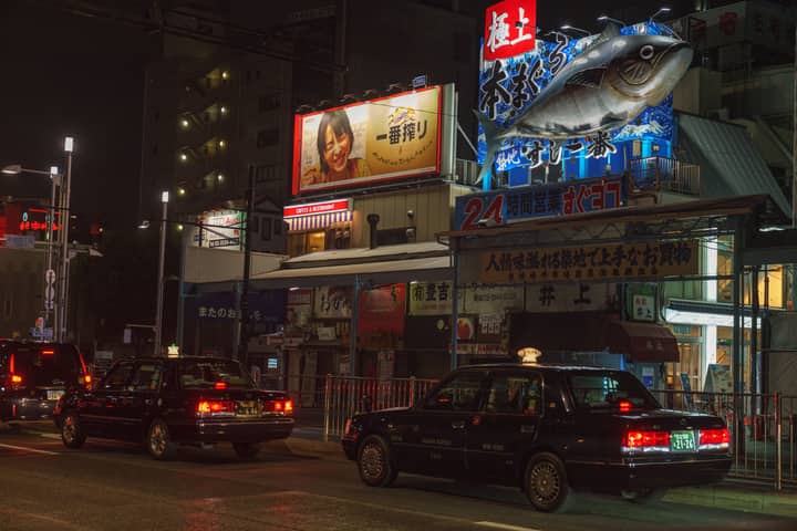 Illuminated street in Chuo City, Tokyo, featuring taxis and vibrant billboards at night.