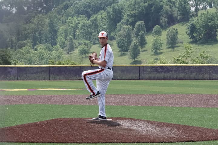 A baseball pitcher prepares to throw on a sunny day at an outdoor field.