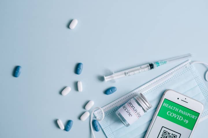 A flat lay of COVID-19 vaccination items including a mask, syringe, and health passport.