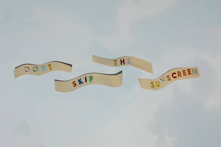 Colorful cutout letters forming a reminder to wear sunscreen against blue sky.