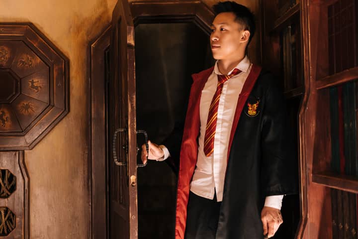 A young man in wizard attire opens a wooden door, creating an air of mystery.