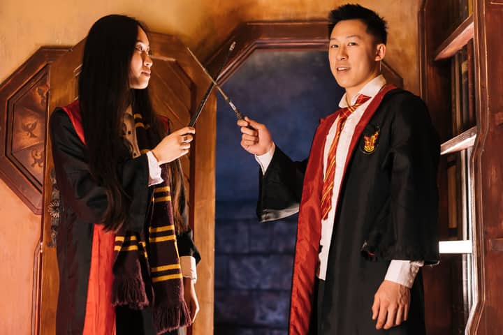 Two young adults dressed as wizards holding wands in a magical setting.