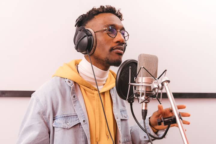 Casual African American man recording music with microphone in professional studio.