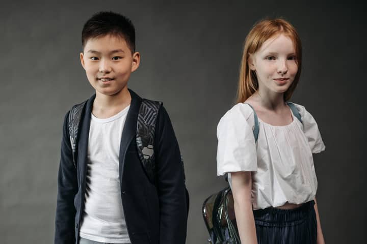 Two schoolchildren smiling with backpacks in a studio setting.