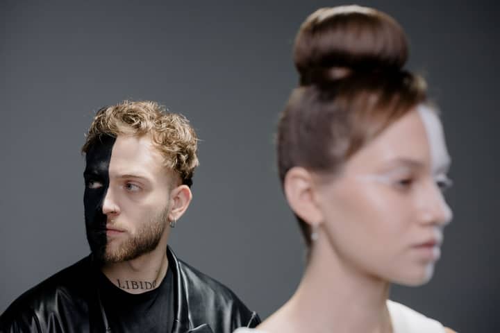 Artistic portrait featuring two models with creative half-face paint against a gray background.