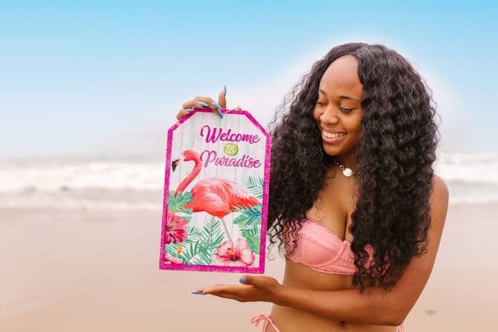 A cheerful woman enjoying a sunny day at the beach, holding a 'Welcome to Paradise' sign.