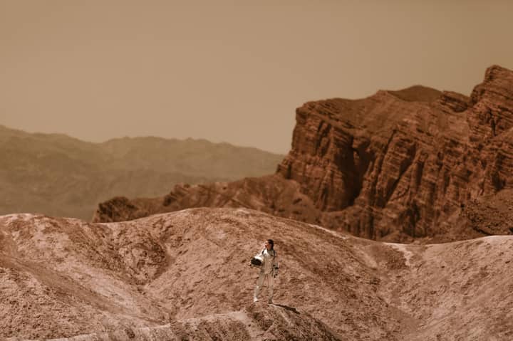 A woman astronaut stands on a barren, alien terrain, symbolizing space colonization.